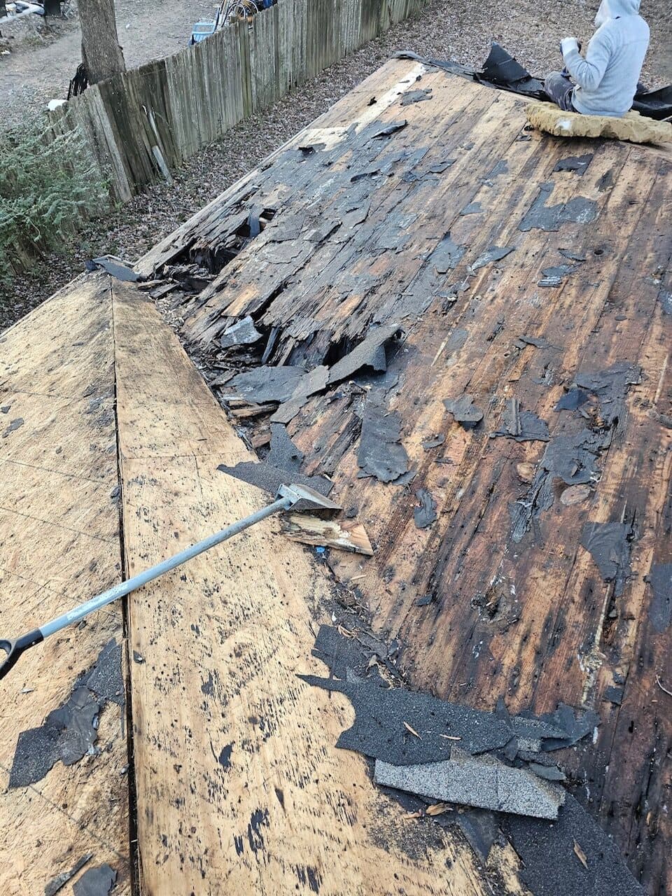 Roof tear-off in progress with old shingles removed down to the plank decking