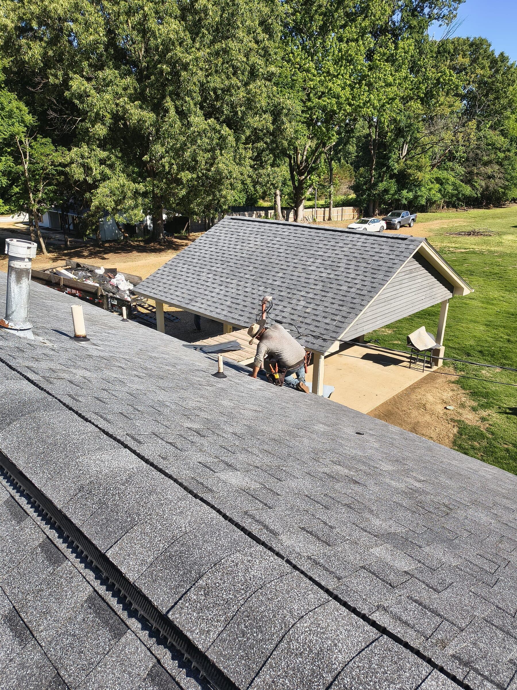 View along a shingle ridge toward crew members working at the far end of the roof