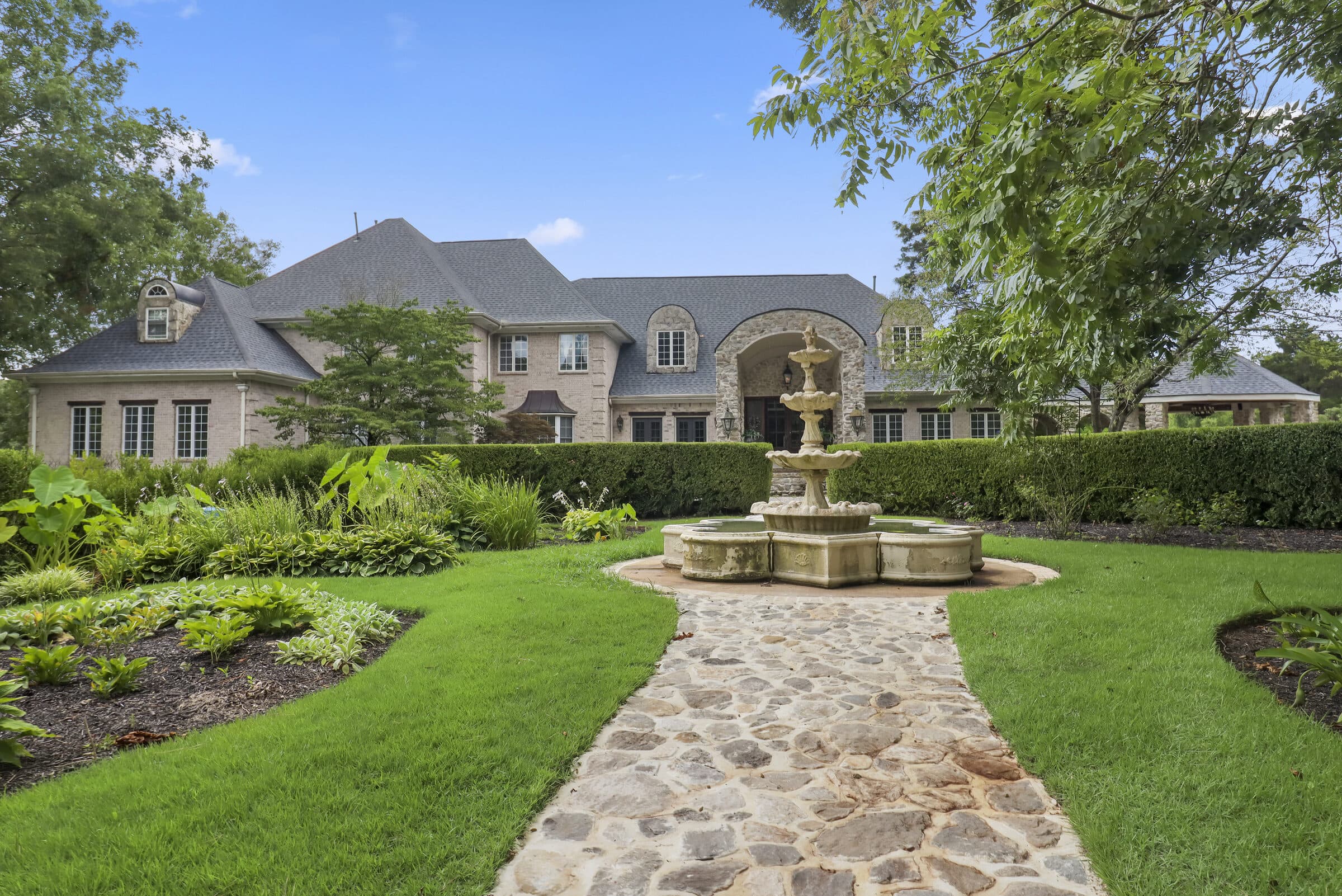 Estate home with a stone fountain and formal garden, completed roof visible