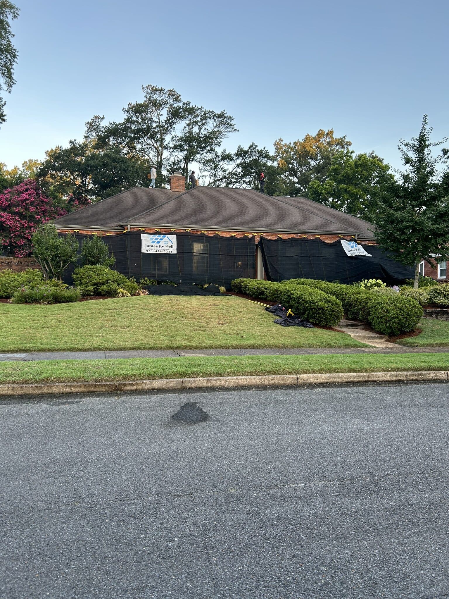 Storm-damaged home protected by black roof tarping with a company sign out front